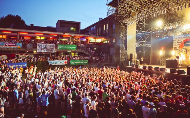 Eine große Menschenmenge genießt ein Konzert vor einer Bühne mit Lichteffekten.