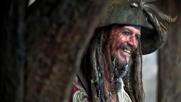 Ein lächelnder Pirat mit Dreispitz und Dreadlocks, möglicherweise Captain Teague aus „Fluch der Karibik“.