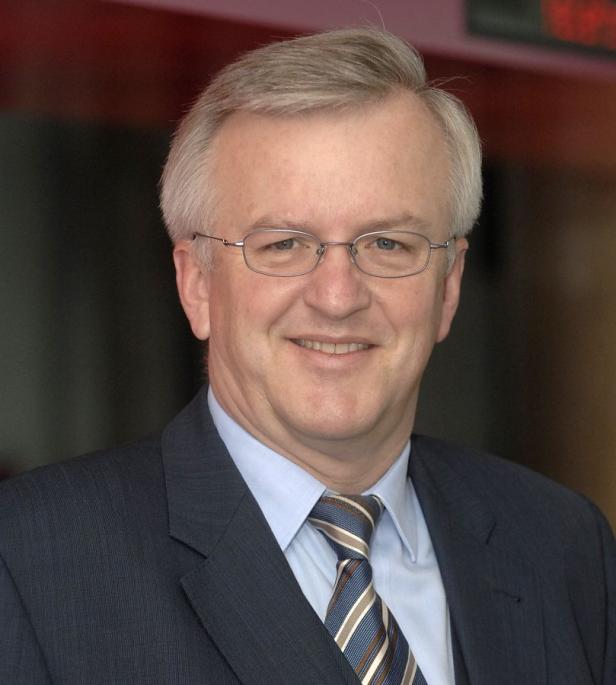 Ein Mann mit Brille, Anzug und Krawatte lächelt in die Kamera.