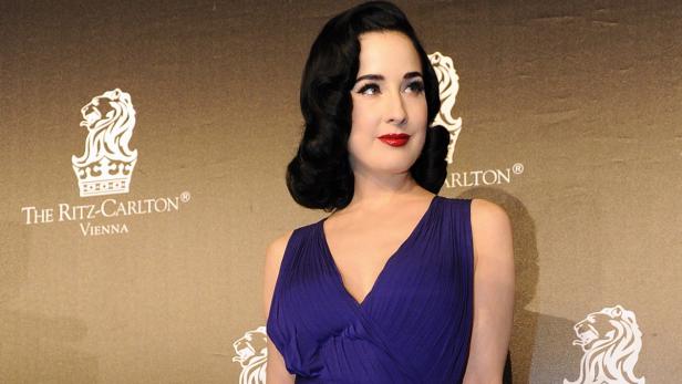 Dita Von Teese in einem lilafarbenen Kleid vor einer Wand des Ritz-Carlton in Wien.