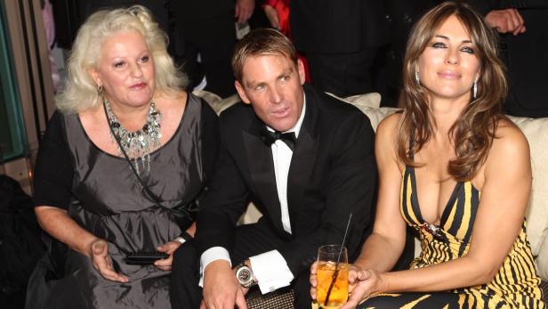 Eine Frau, Shane Warne und Elizabeth Hurley sitzen zusammen auf einem Sofa.