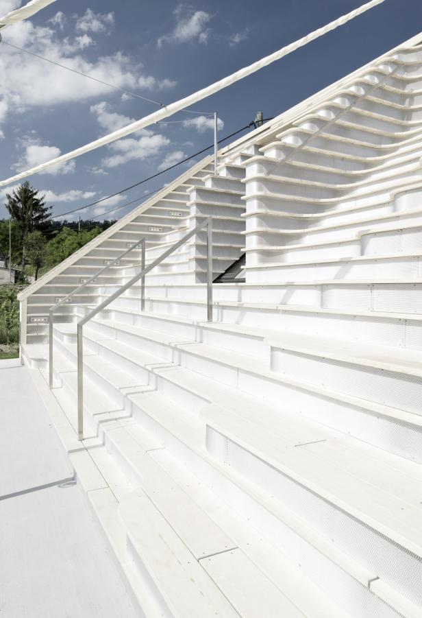 Eine weiße Treppe mit Metallgeländer führt zu einem Gebäude unter blauem Himmel.