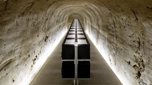 Ein langer Tisch mit schwarzen Kisten steht in einem Tunnel mit rauen Wänden.
