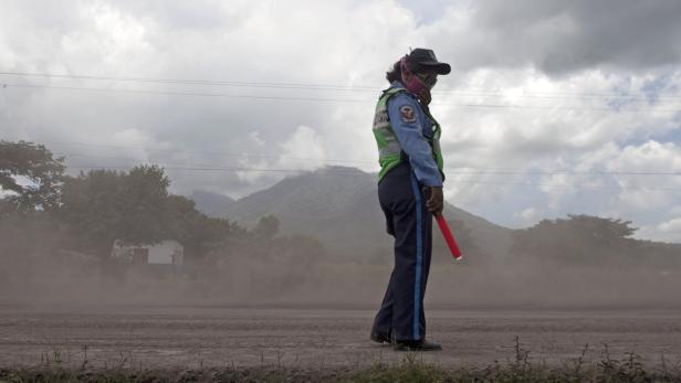 Eine Verkehrspolizistin steht in einer staubigen Umgebung mit einem roten Leuchtstab.