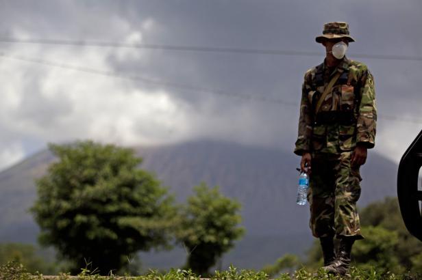 Ein Soldat mit Tarnuniform und Gesichtsmaske steht vor einem bewölkten Himmel und einem Berg.