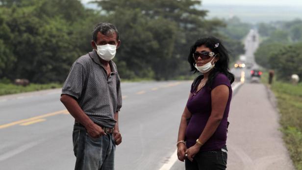 Ein Mann und eine Frau stehen mit Gesichtsmasken an einer Landstraße.