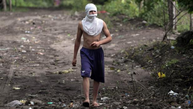 Ein junger Mann mit bedecktem Gesicht geht auf einer schmutzigen Straße entlang.