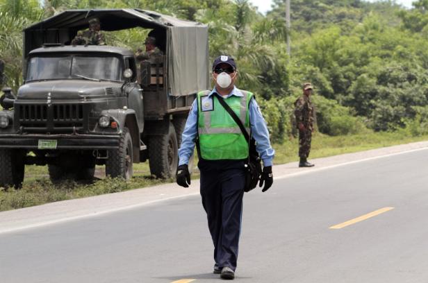 Ein Mann mit Maske und Warnweste geht auf einer Straße entlang, im Hintergrund ein Militärfahrzeug.