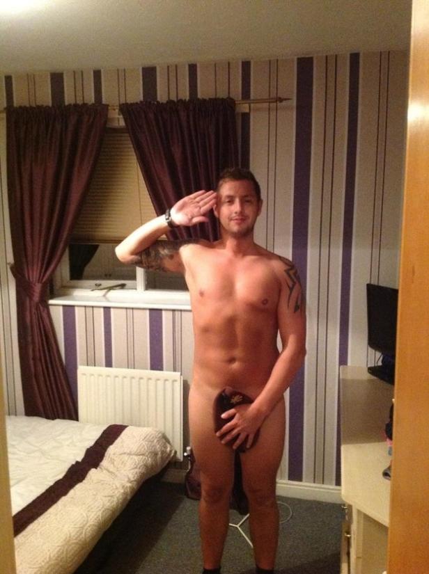 Ein Mann steht in einem Schlafzimmer und salutiert, während er sich mit einem Tuch bedeckt.