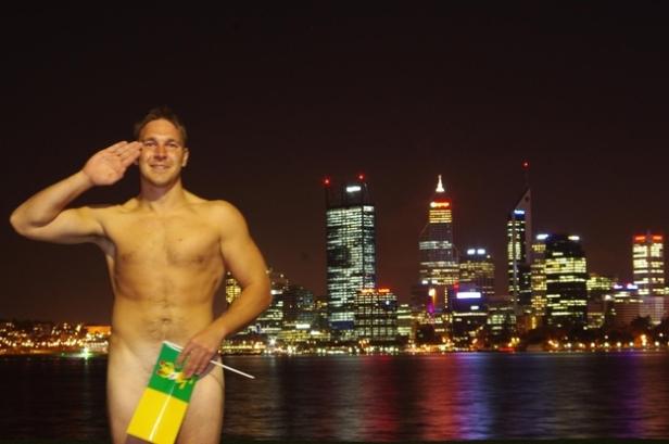 Ein Mann salutiert mit einer Flagge vor der Skyline von Perth bei Nacht.