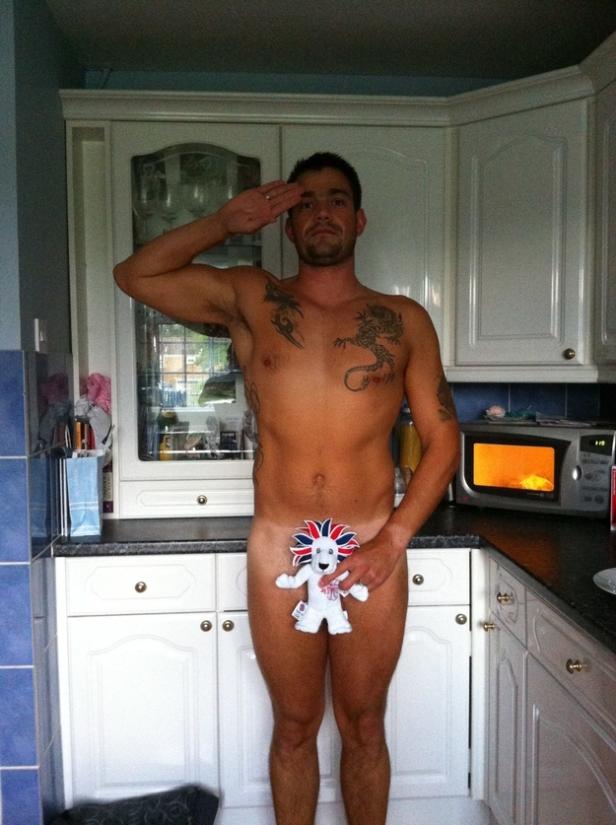 Ein Mann mit Tätowierungen salutiert, während er in einer Küche mit einem Stofftier posiert.