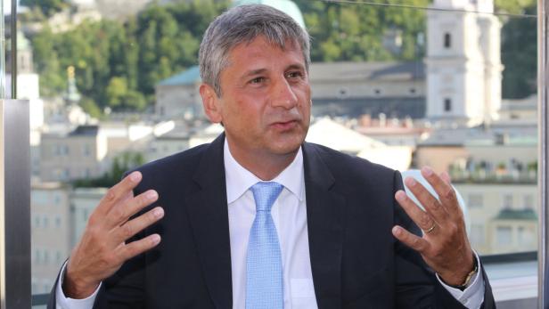 Ein Mann in Anzug gestikuliert vor einem Gebäude in Salzburg.