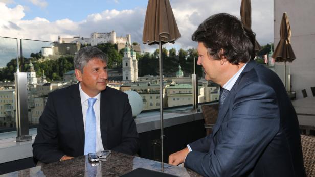 Zwei Männer in Anzügen sitzen auf einer Terrasse mit Blick auf Salzburg.