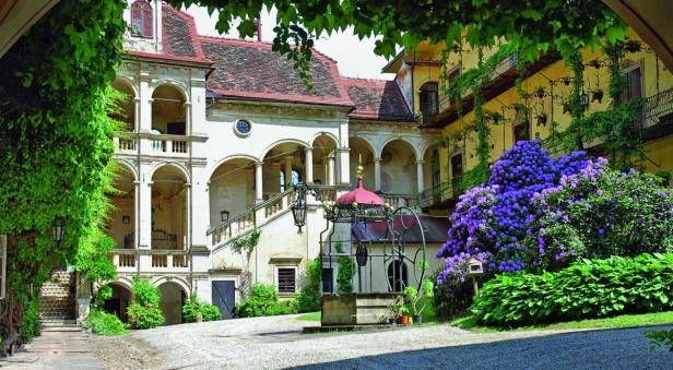 Ein Innenhof eines Schlosses mit einem Brunnen und blühenden Rhododendren.