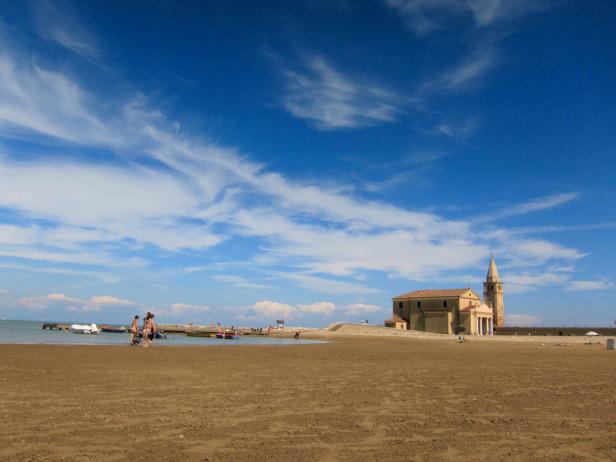 Eine Kirche mit Glockenturm steht an einem sonnigen Strand.