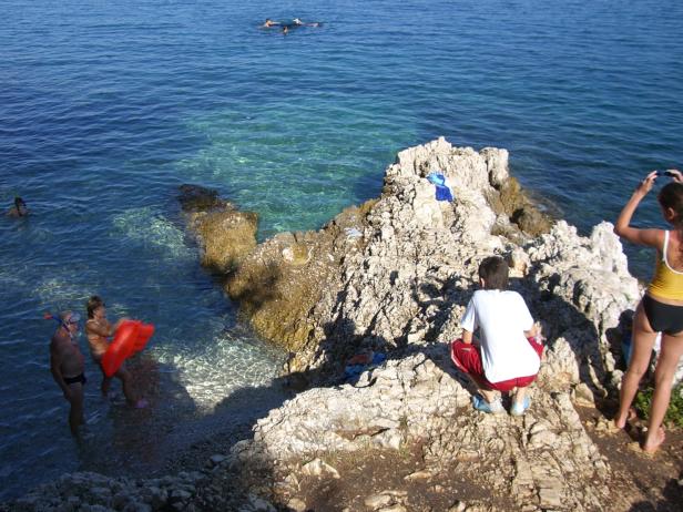 Menschen genießen das klare Wasser an einer felsigen Küste.