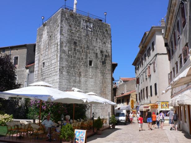 Ein belebter Platz in Bale, Kroatien, mit einem alten Steinturm und Cafés.