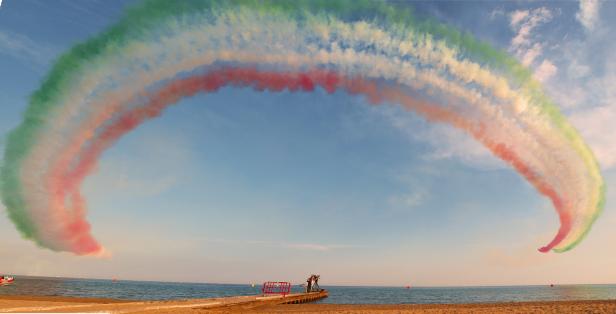 Ein Rauchbogen in den Farben der italienischen Flagge über einem Strand.