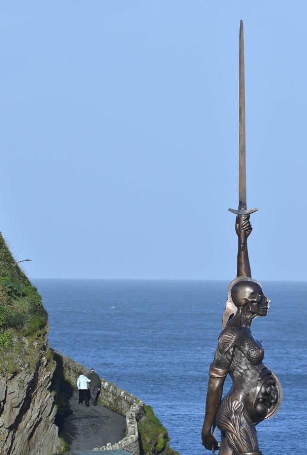 Eine Bronzeskulptur einer Frau mit Schwert vor dem Meer.