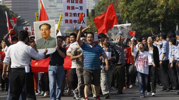 Eine Menschenmenge demonstriert mit chinesischen Flaggen und einem Porträt von Mao Zedong.