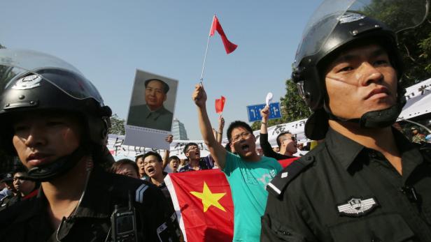 Polizisten stehen vor einer Menschenmenge mit chinesischen Flaggen und einem Mao-Porträt.
