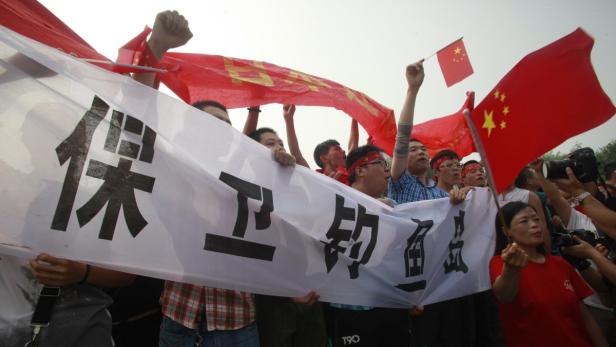 Eine Gruppe von Menschen demonstriert mit chinesischen Flaggen und einem Banner.