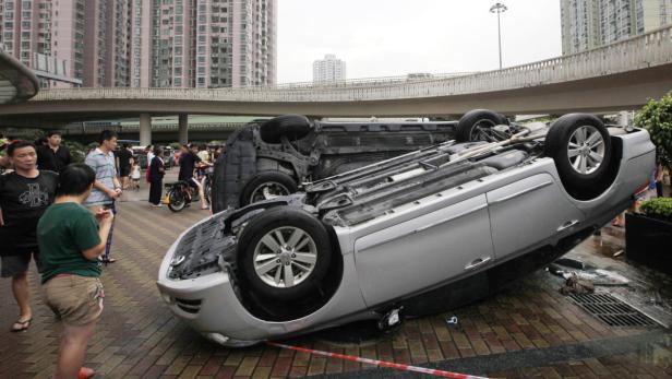 Ein auf dem Dach liegendes Auto wird von einer Menschenmenge in einer städtischen Umgebung betrachtet.