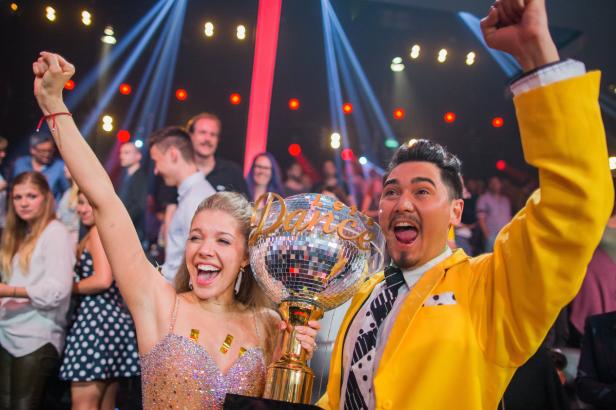 Ein tanzendes Paar hält freudestrahlend eine Discokugel-Trophäe in die Höhe.