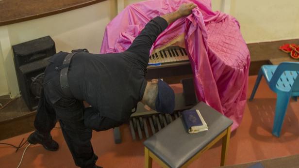 Ein Mann deckt ein Klavier mit einem rosa Tuch ab.
