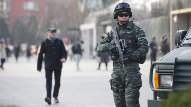 Ein Soldat in Tarnuniform steht mit einem Gewehr auf einer belebten Straße.