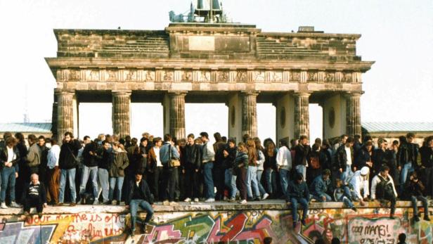 Menschen stehen auf der Berliner Mauer vor dem Brandenburger Tor.