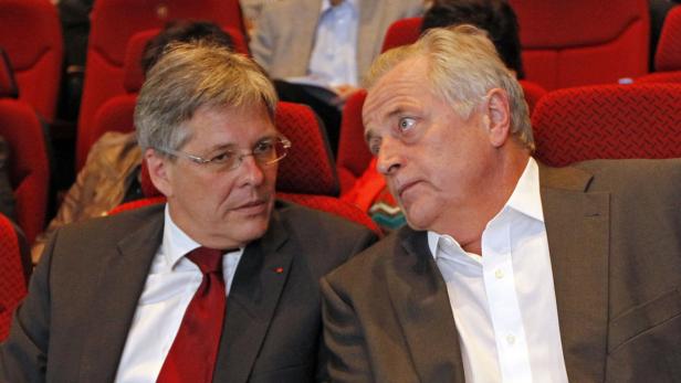 Zwei Männer in Anzügen unterhalten sich in einem Theatersaal.