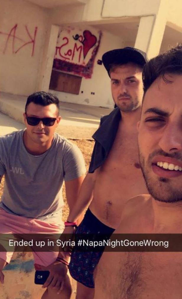 Drei junge Männer machen ein Selfie vor einer Wand mit Graffiti, möglicherweise in Syrien.