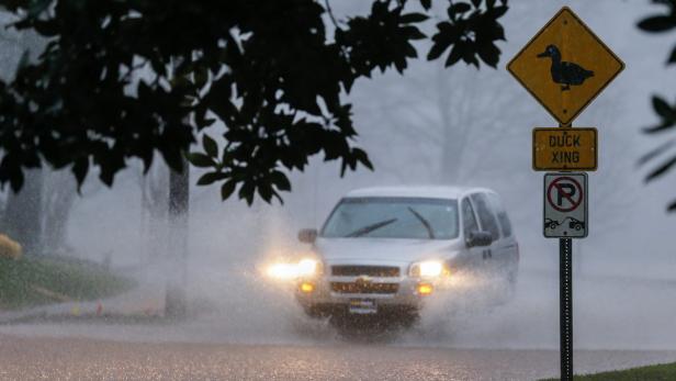 Ein Auto fährt durch eine überflutete Straße an einem „Enten überqueren“-Schild vorbei.