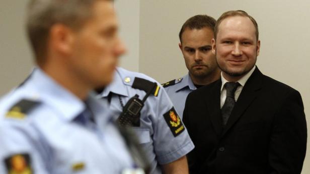 Der Massenmörder nahm das Urteil mit einem Lächeln zur Kenntnis. Anders Behring Breivik lächelt, während er von Polizisten umgeben ist.