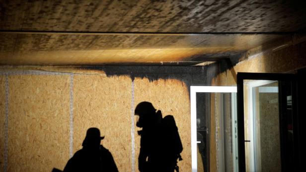 Die Schatten zweier Personen, möglicherweise Feuerwehrleute, in einem Raum mit Brandschäden.