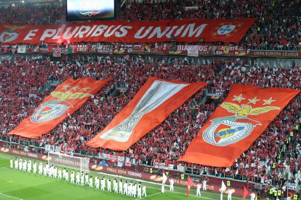 Fußballfans schwenken große Banner mit dem Benfica-Logo und dem Schriftzug „E Pluribus Unum“.
