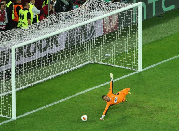 Ein Torwart hechtet nach einem Fußball vor einem Tor.