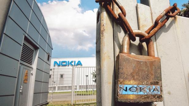 Ein verrostetes Vorhängeschloss und eine Kette versperren ein Tor vor einem Nokia-Gebäude.