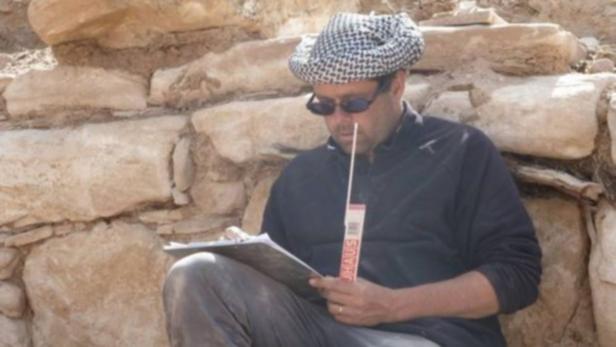 Ein Mann mit Kufiya und Sonnenbrille macht sich Notizen vor einer Steinwand.