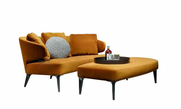 Sofa 'Aston' ist Teil der neuen Kollektion für Minotti. Ein ockerfarbenes Sofa mit Ottoman, darauf eine Flasche und ein Glas auf einem Tablett.