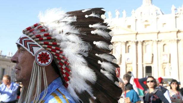 Ein Mann mit traditionellem Kopfschmuck vor einem Gebäude mit Säulen.