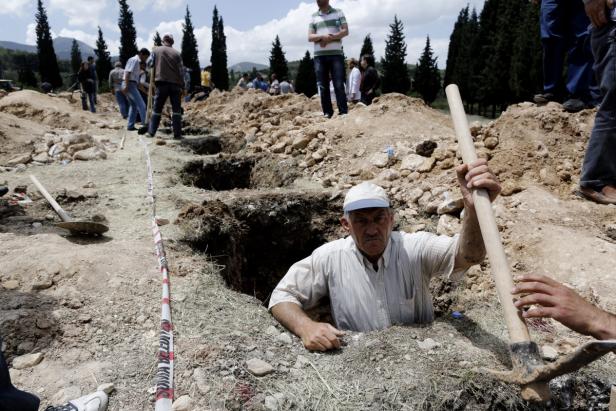 Ein Mann steht in einem Erdloch und hält eine Spitzhacke.