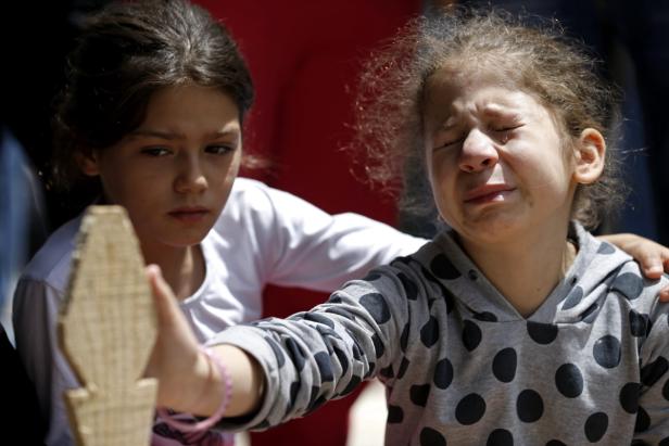 Ein Mädchen weint, während ein anderes Mädchen daneben steht und einen Holzkreuz hält.