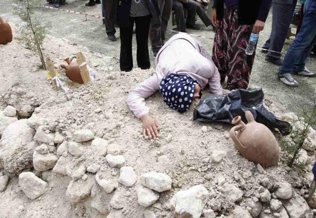 Eine Frau liegt weinend auf einem Grabhügel.