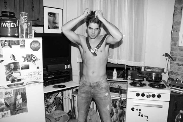 Ein junger Mann steht in einer Küche und hält sich die Haare hoch.