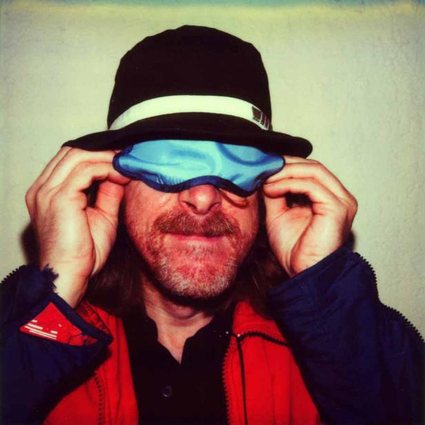 Ein Mann mit Hut und Schlafmaske vor den Augen.