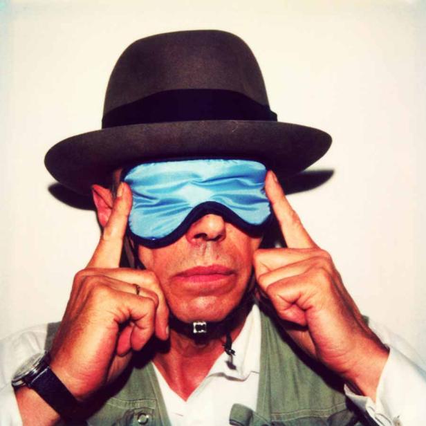 Ein Mann mit Hut und Schlafmaske vor den Augen posiert.