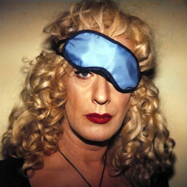 Eine Frau mit blonden Locken und rotem Lippenstift trägt eine blaue Schlafmaske.