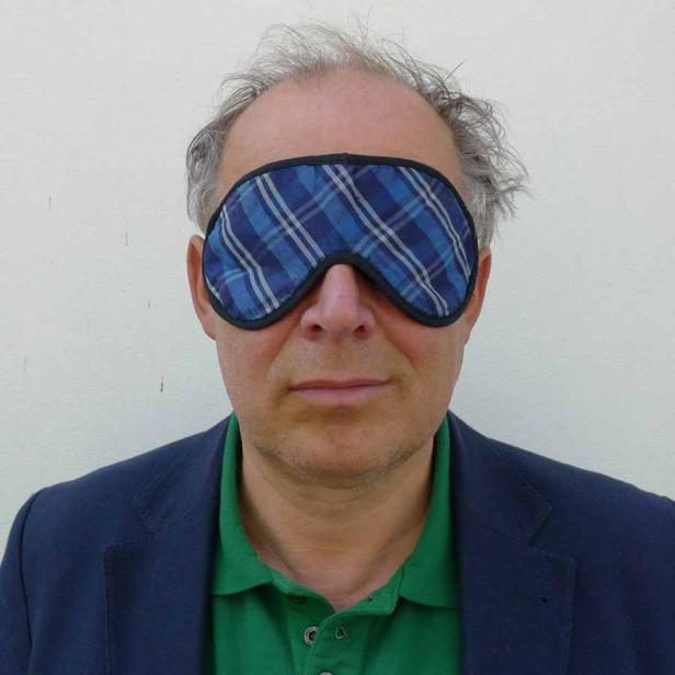 Ein Mann mit Schlafmaske vor einer weißen Wand.